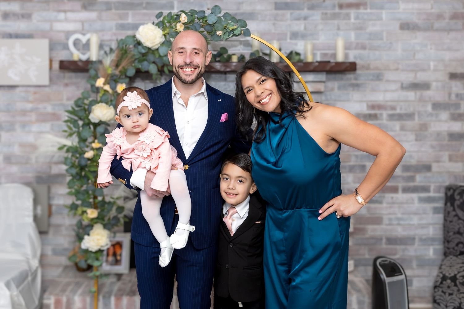 Happy family of four posing before floral arch backdrop at formal celebration event.