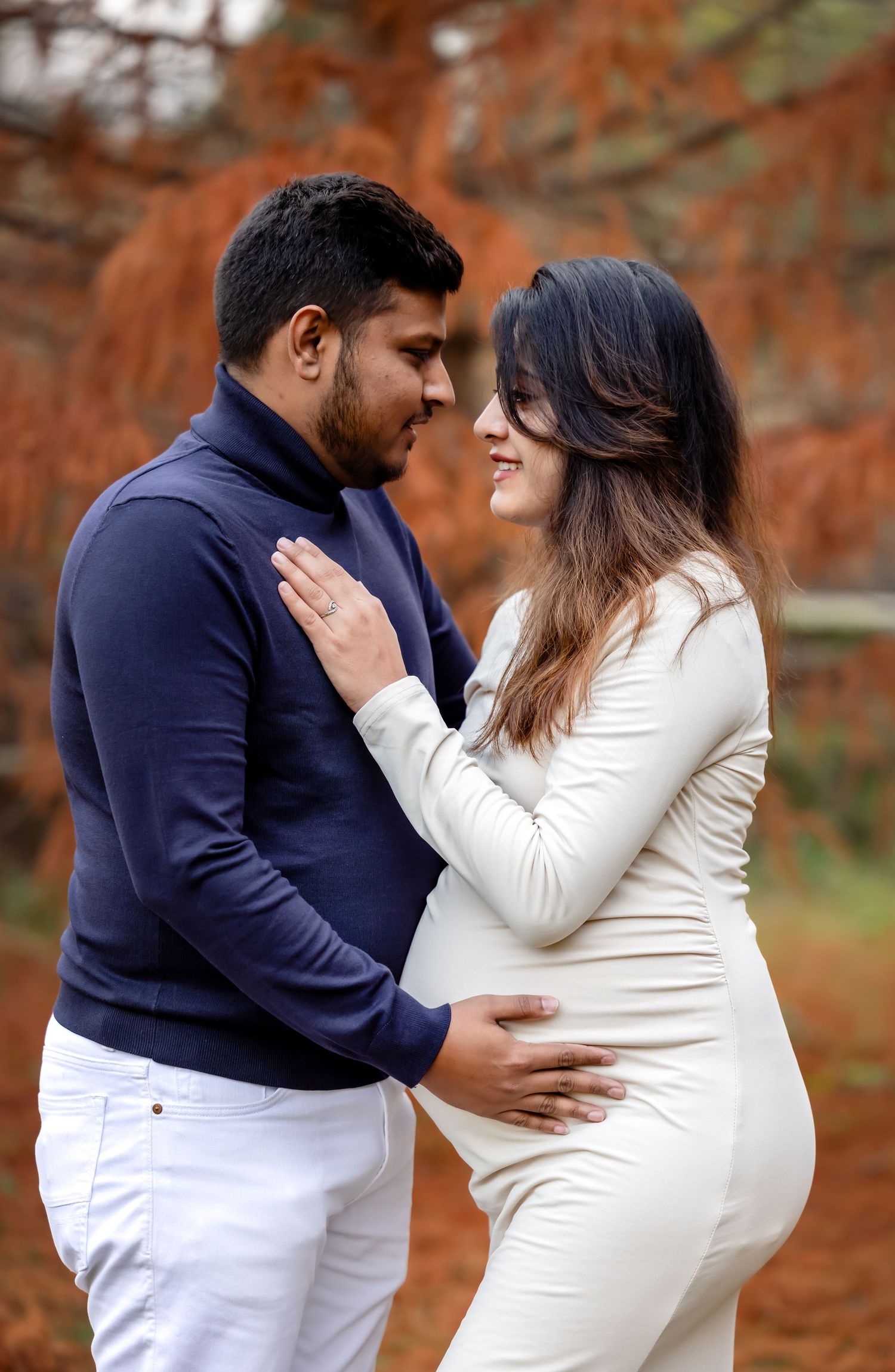 Loving couple sharing tender moment during autumn maternity photoshoot in park.