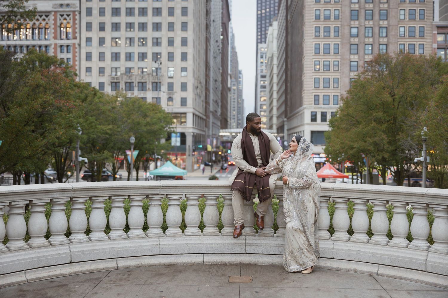 Muslim bride and groom in traditional attire stand on white stone bridge in downtown Chicago.