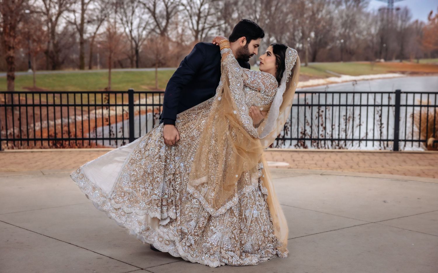 Groom dipping bride in gold embroidered lehenga in romantic outdoor wedding photo.