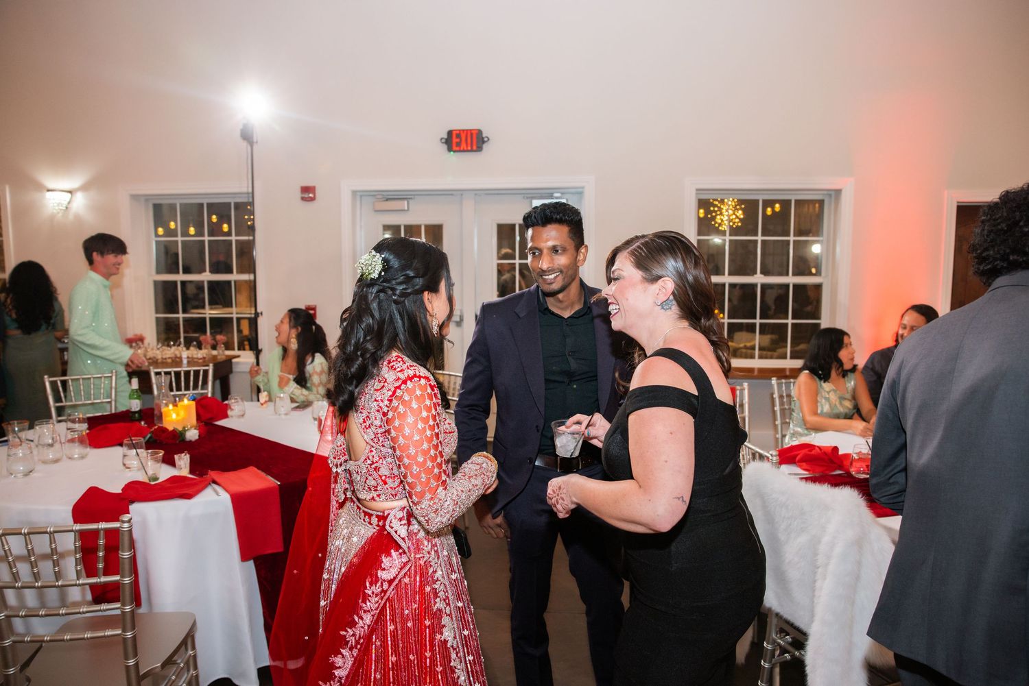 Guests in formal attire mingle at an elegant wedding reception with red table settings.