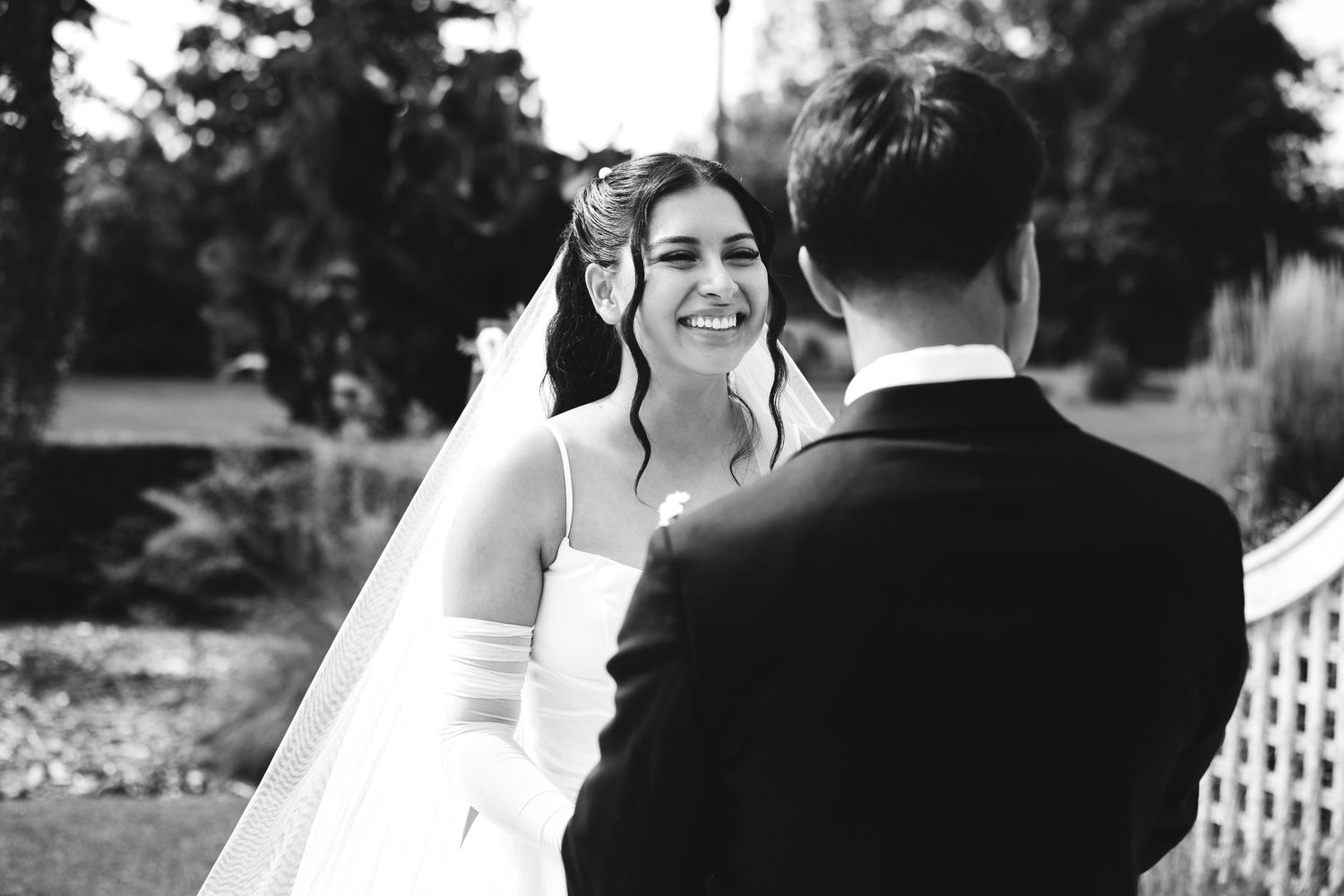 Bride smiling joyfully at groom during outdoor wedding ceremony in black and white photo.