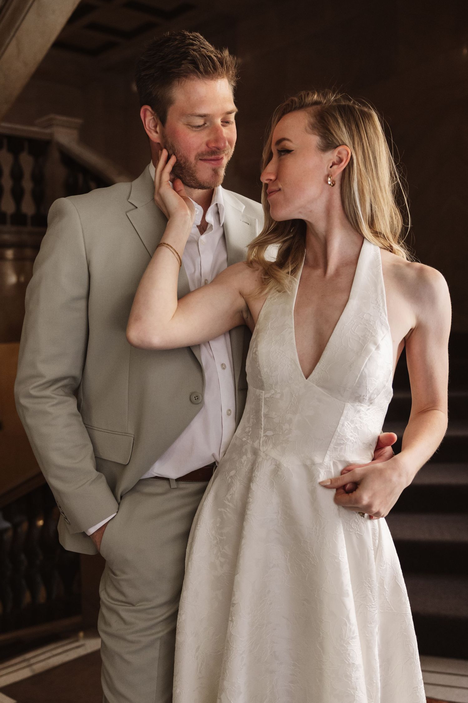 Bride in white gown tenderly cups groom's face in a romantic indoor wedding portrait.