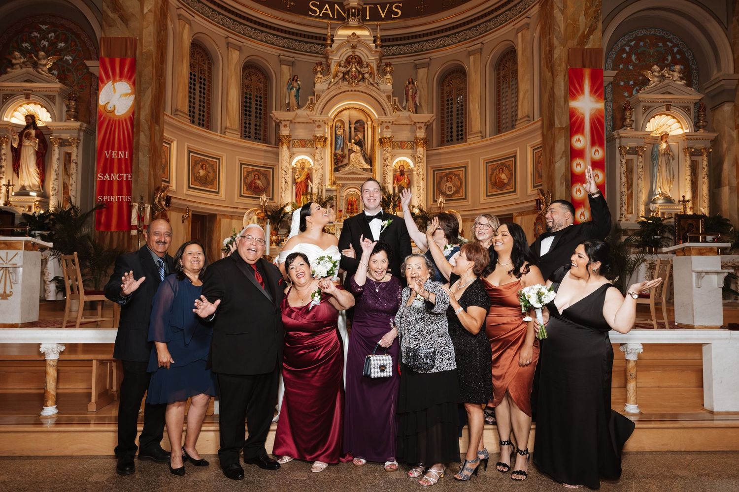 Wedding party poses joyfully in front of an ornate church altar after the ceremony.