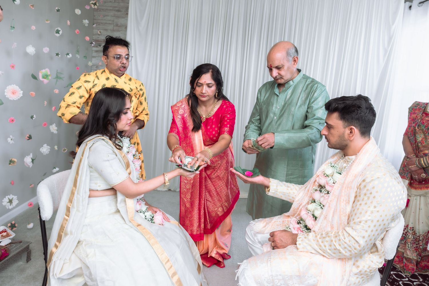 Family members perform a traditional Indian wedding ritual as the bride and groom sit during a ceremonial exchange.