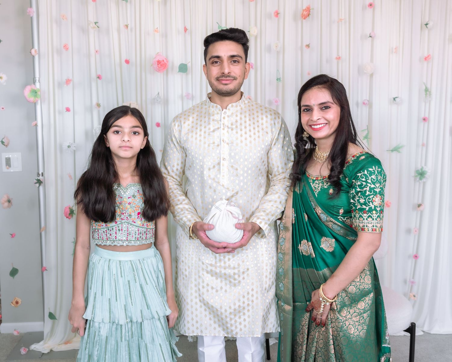 South Asian family of three posing in traditional Indian attire at festive celebration event.