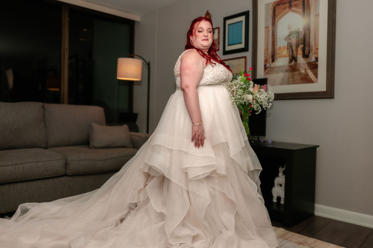 A plus-size bride with red hair showcases the full train of her layered white wedding gown.