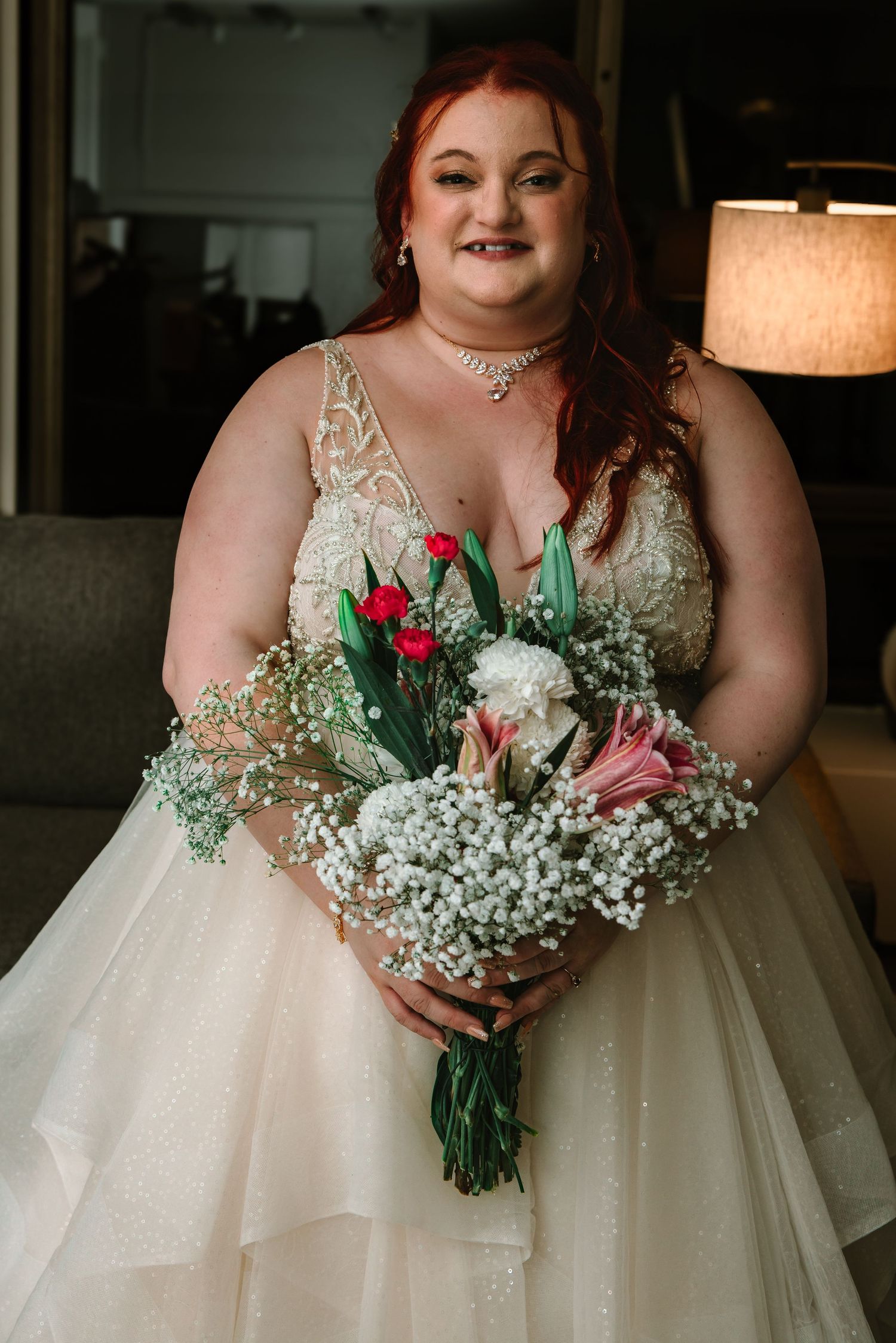 Smiling bride in jeweled lace wedding dress holds colorful bridal bouquet with red tulips.