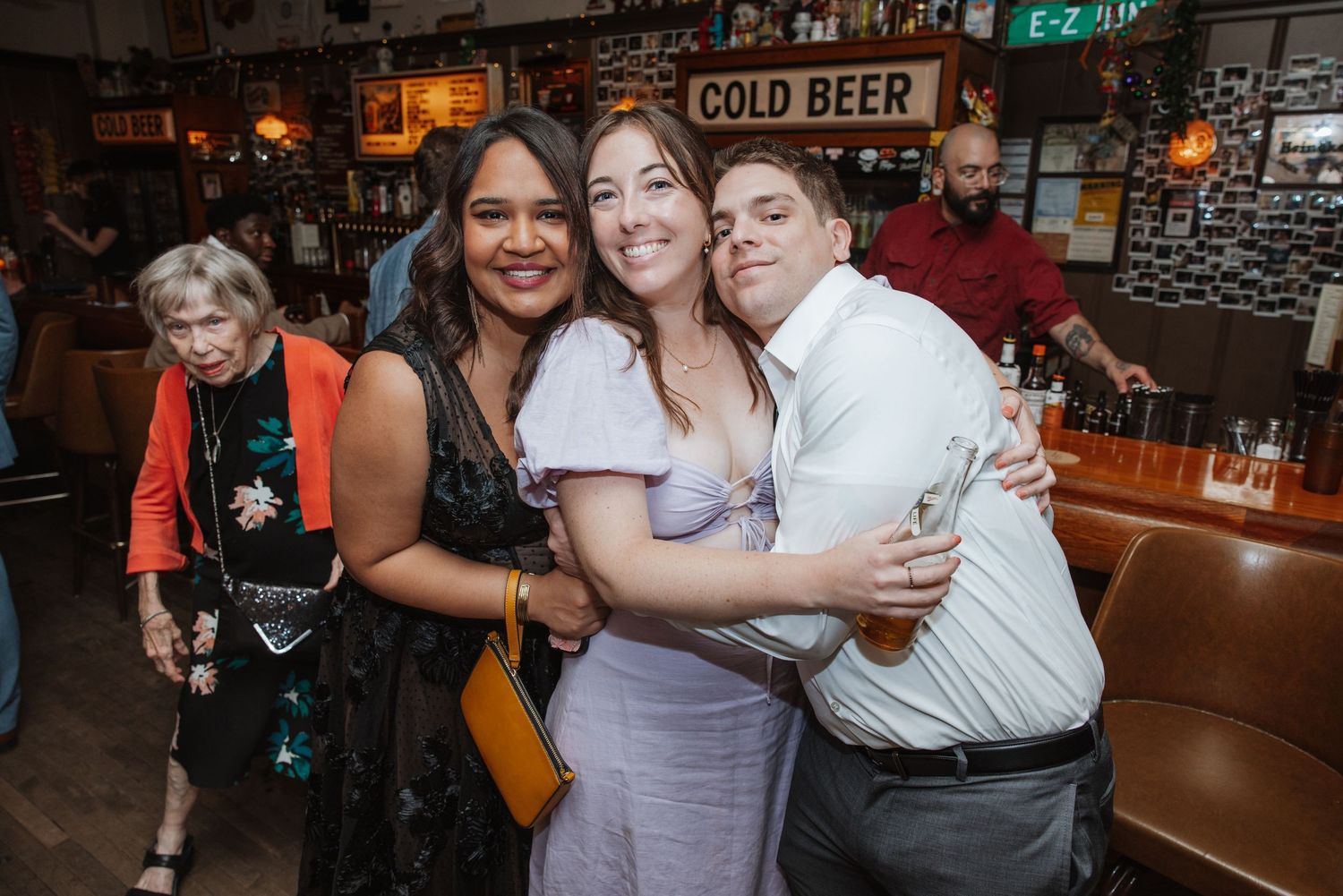 Three friends hugging and smiling together at a casual bar wedding reception event.