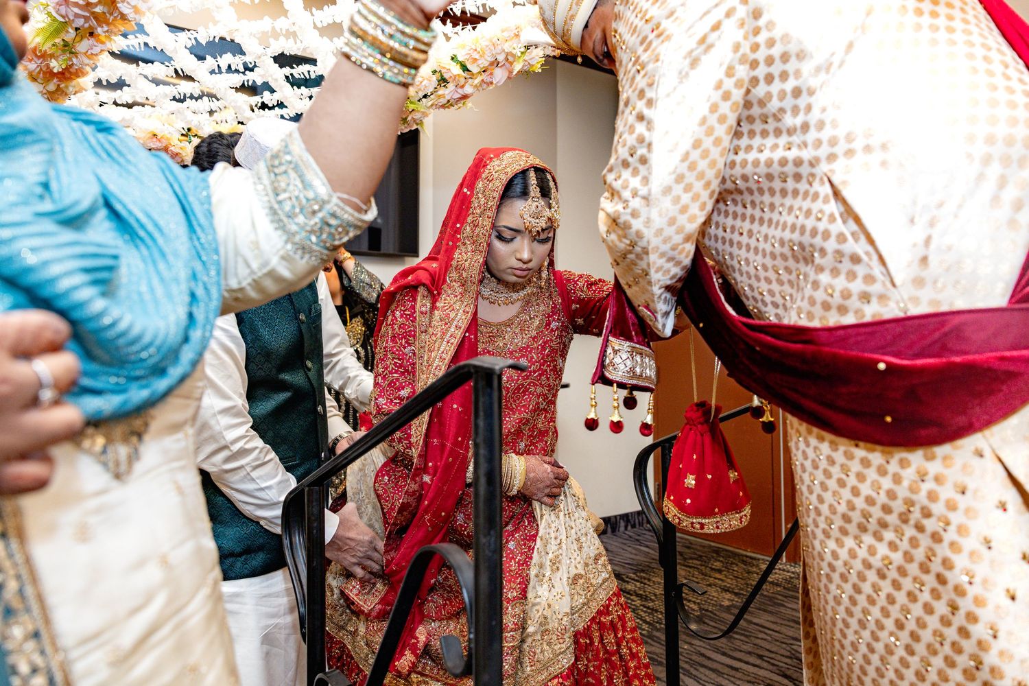 South Asian bride in red and gold bridal lehenga descending stairs at traditional wedding ceremony.
