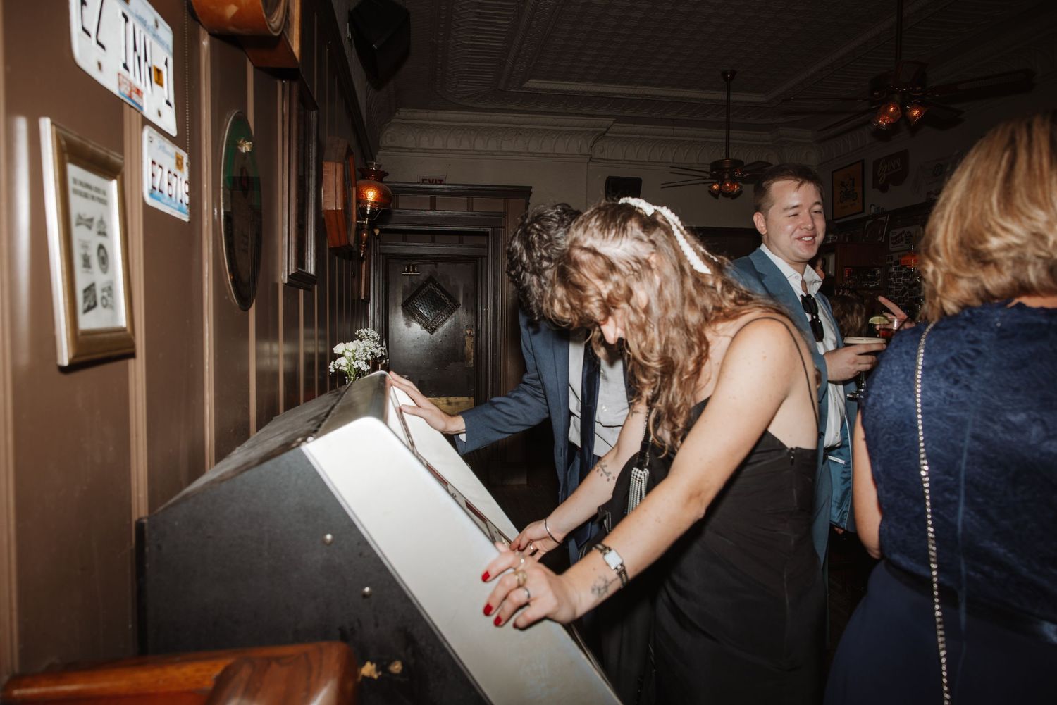 Woman signing a guestbook at a wooden bar while guests mingle in a warmly lit pub.