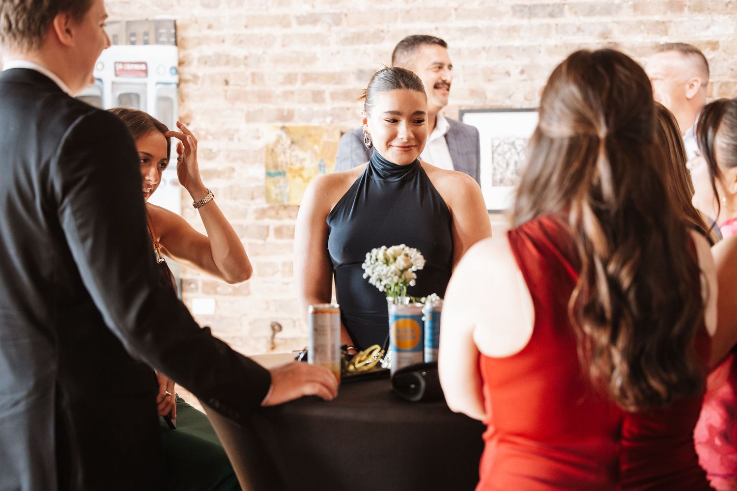 Woman in black halter dress standing at a table during a formal indoor event.