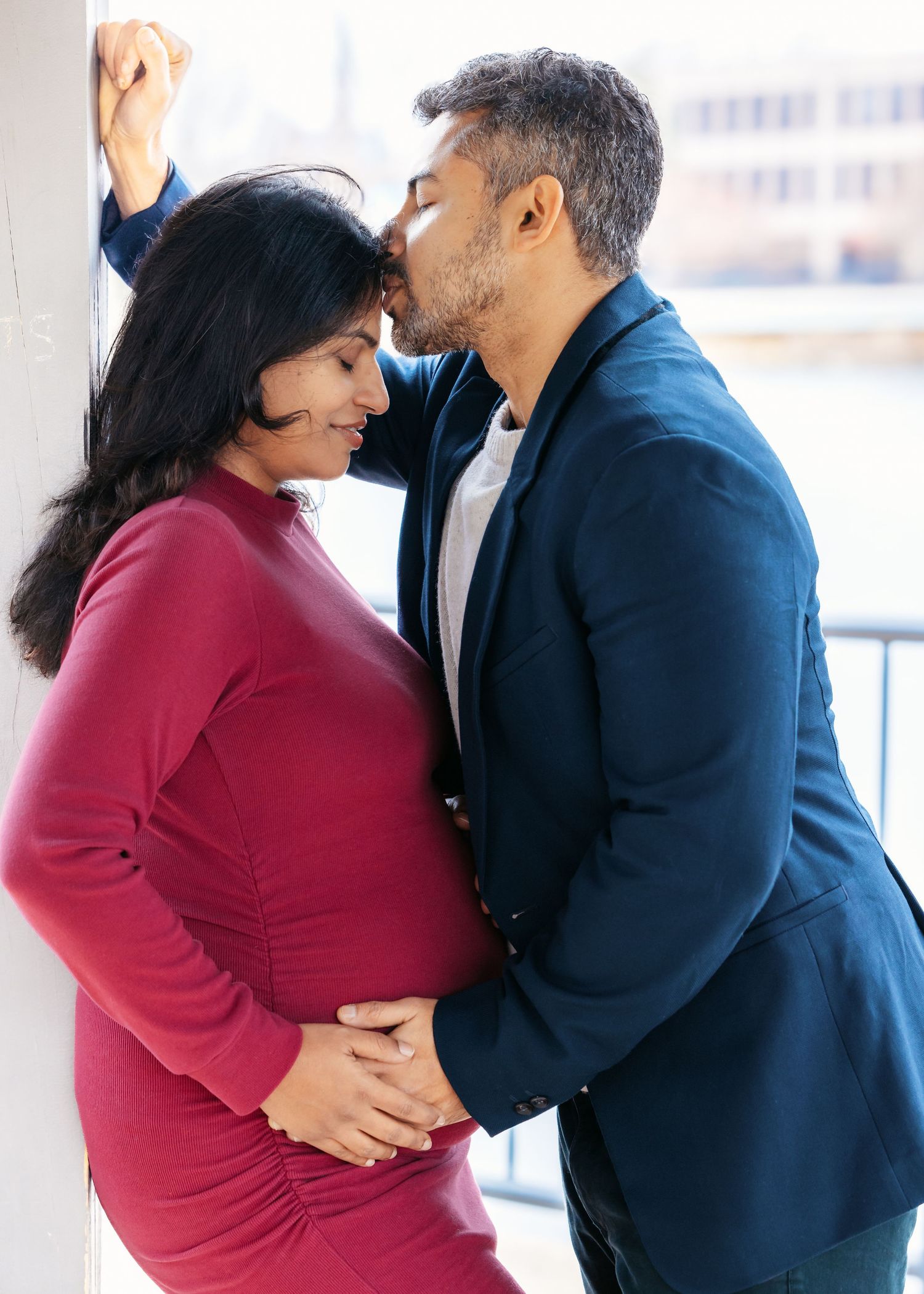 Man tenderly kissing pregnant woman on forehead while holding her belly.