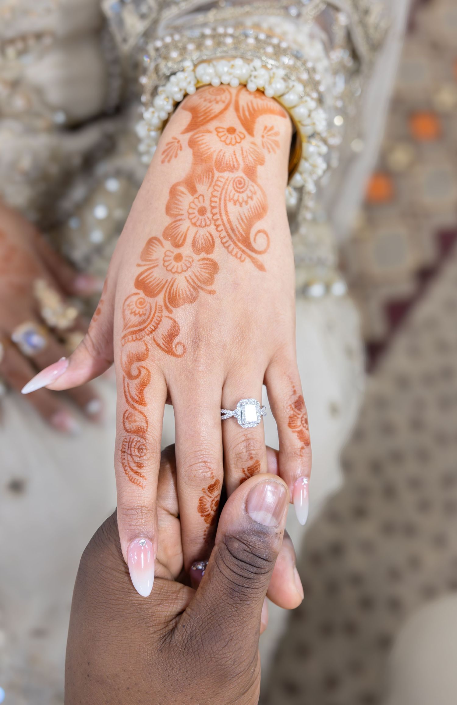Close-up of bride's hand with intricate henna mehndi design and diamond engagement ring held by groom.