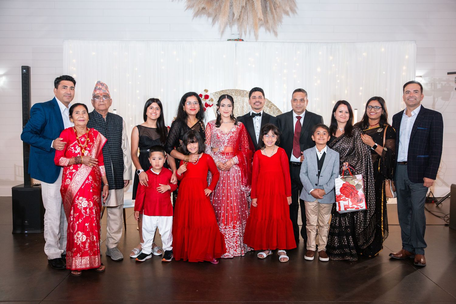 Large family group photo with bride in red lehenga at elegant Indian wedding reception.