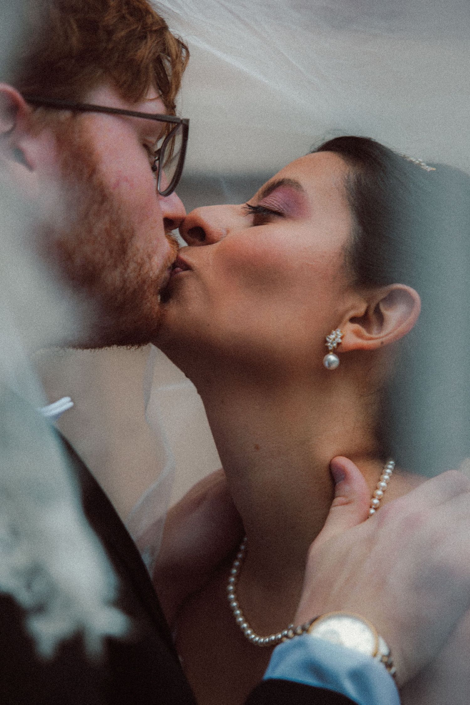 Bride and groom sharing a romantic kiss under a flowing white wedding veil.