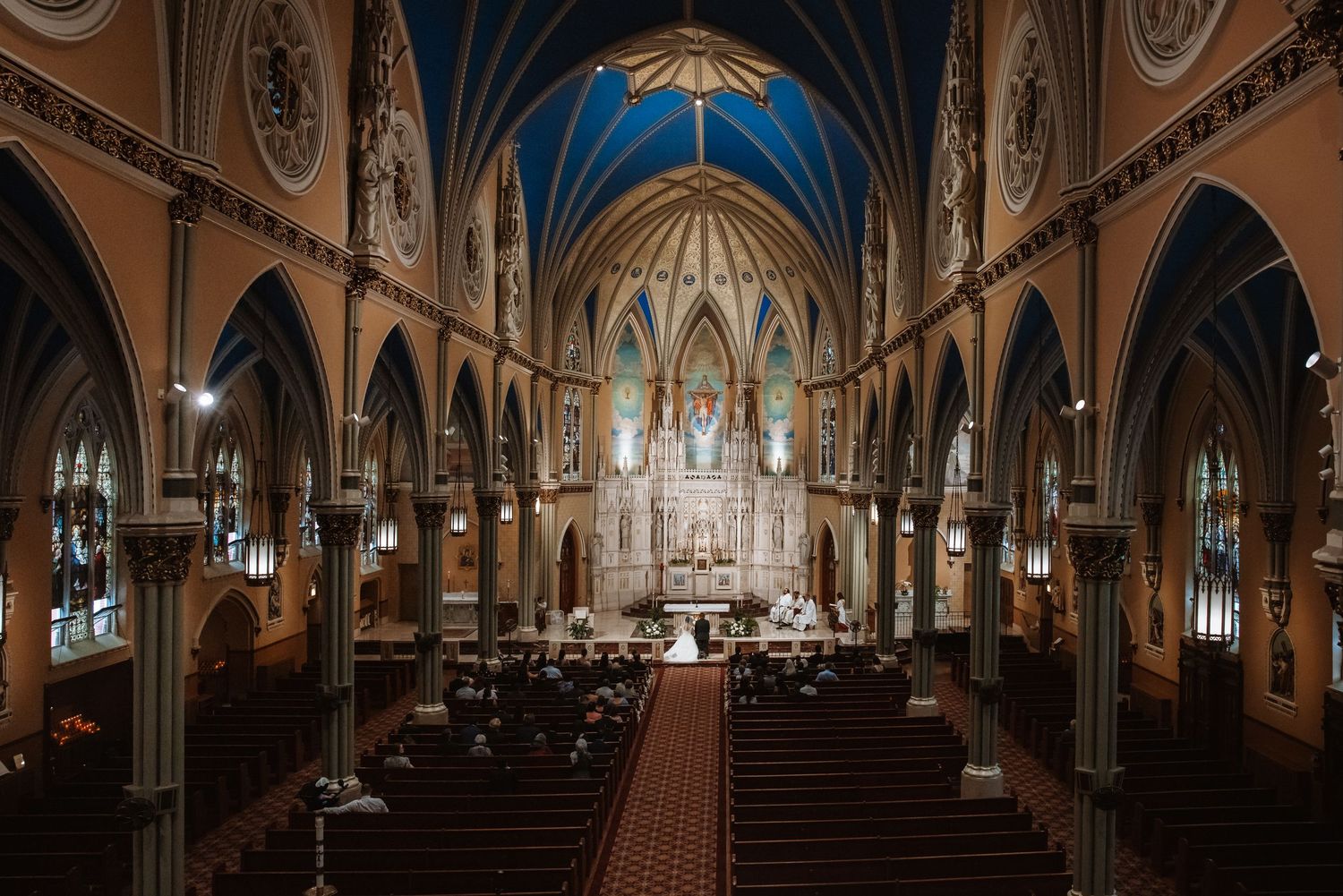Aerial view of elegant Gothic Catholic church nave filled with wedding guests during ceremony.
