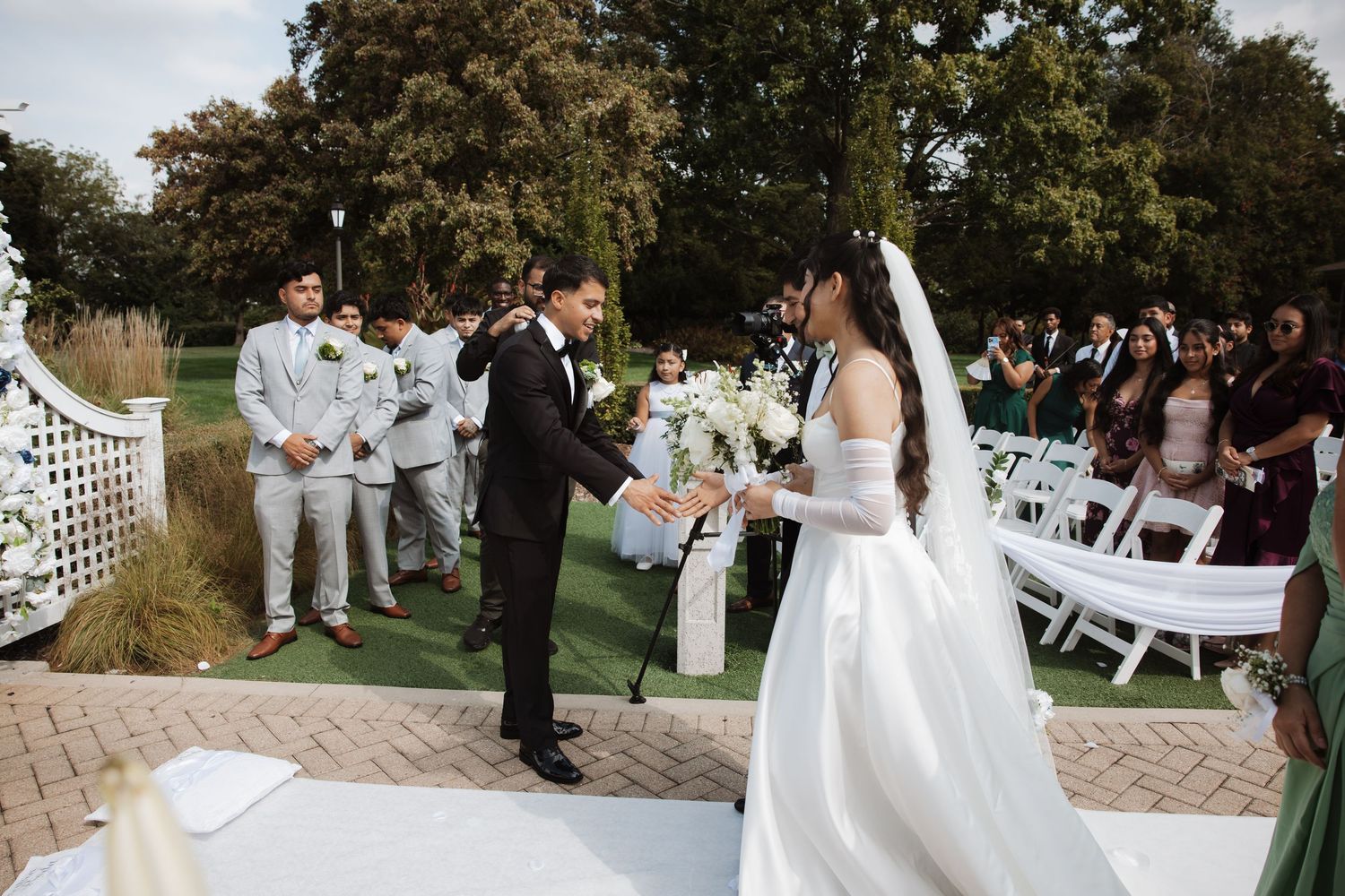 Groom takes bride's hand at the altar during an elegant outdoor wedding ceremony with seated guests.