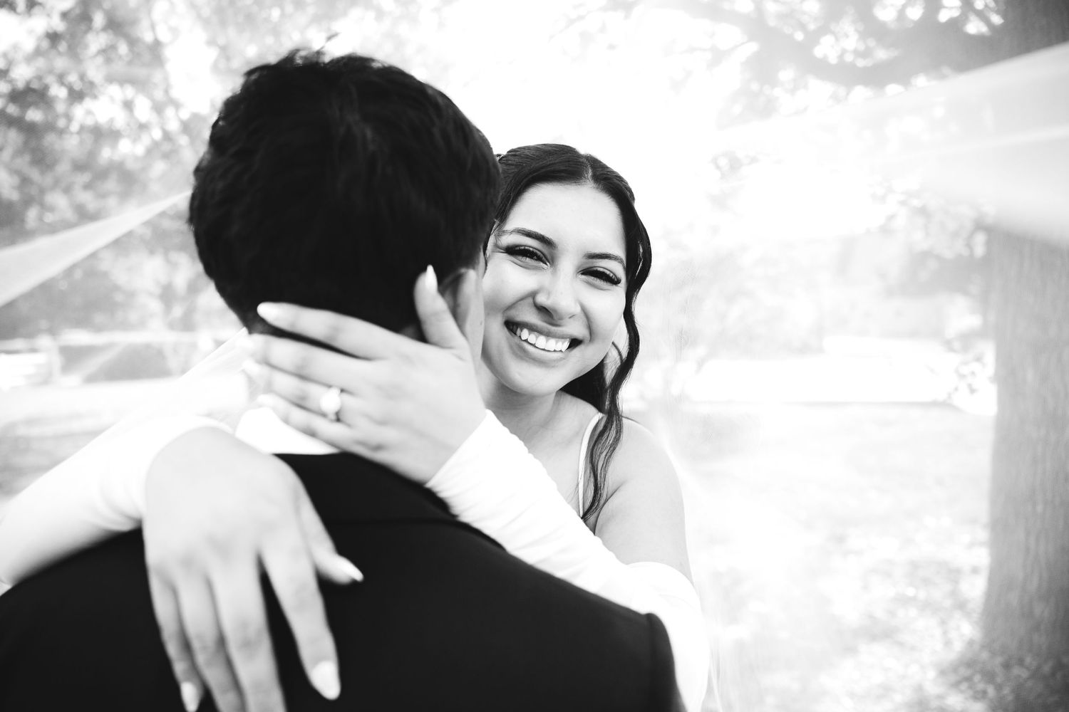Joyful bride in black and white photo embracing groom and smiling radiantly on wedding day.