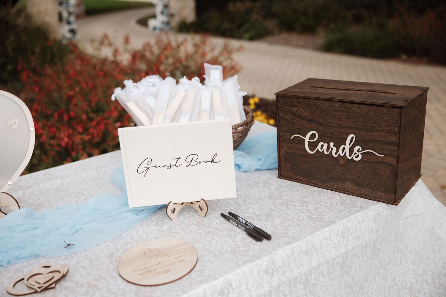 Wedding guest book table with cards box, pen, and white floral decorations outdoors.