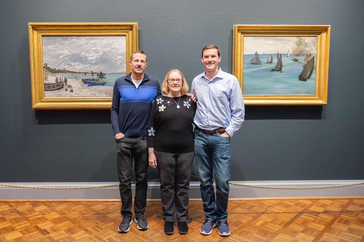 Three people posing together in front of Monet paintings at an art museum.
