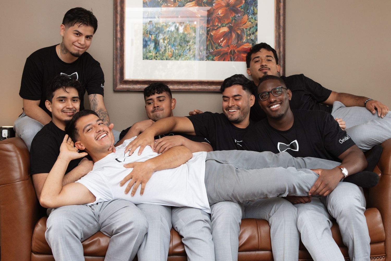 Groom and groomsmen laughing and joking around together on leather sofa during fun pre-wedding preparations.