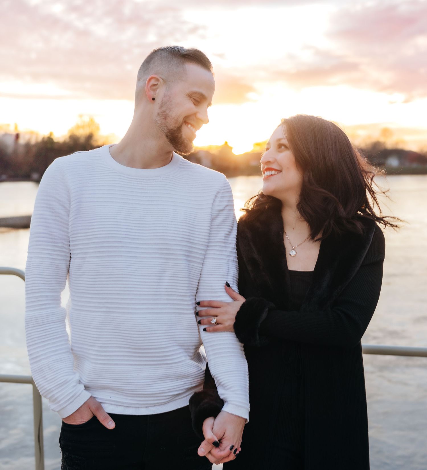 Happy couple holding hands and smiling at each other during a beautiful waterfront sunset.