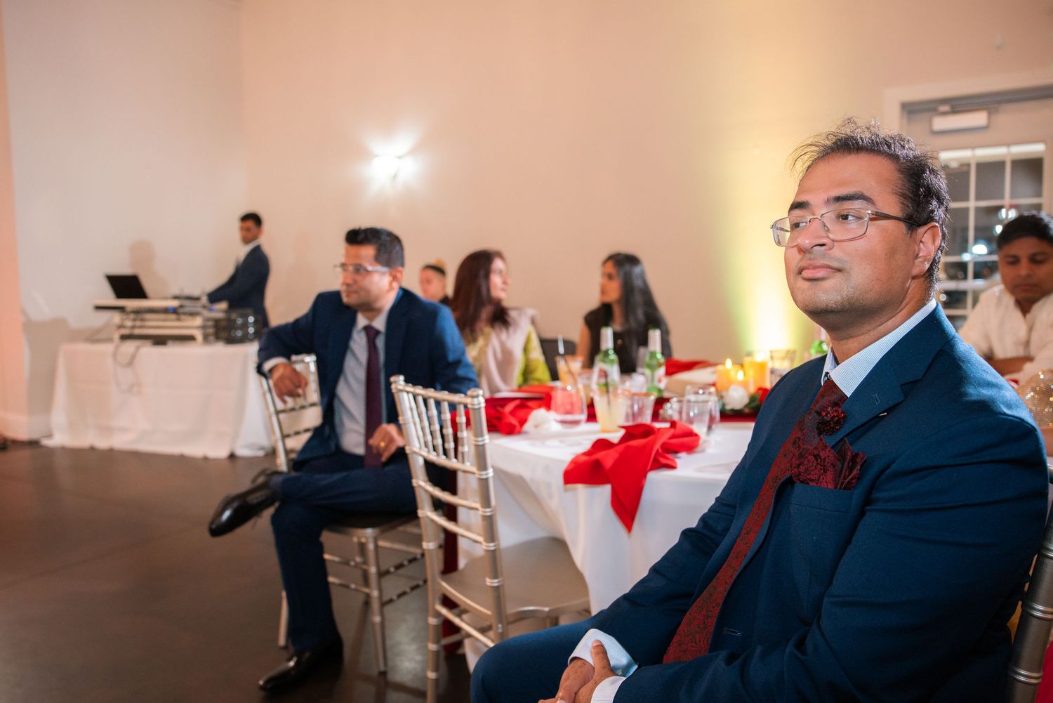Man in navy suit seated at elegant wedding reception venue.