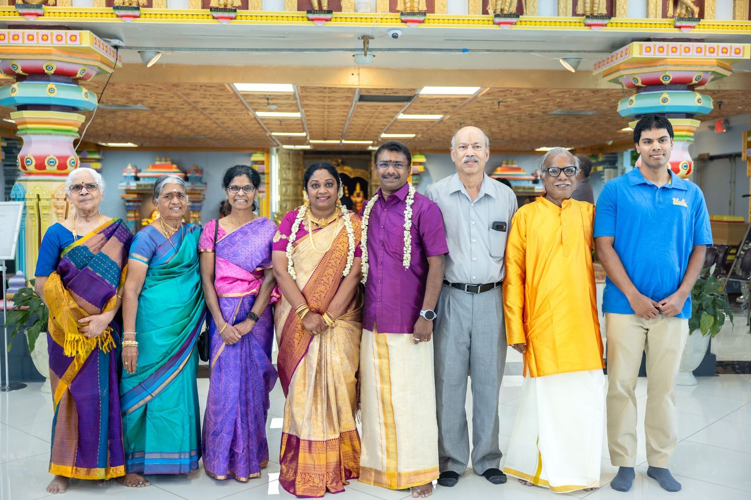 Group of eight people in traditional South Indian attire posing together inside a colorful Hindu temple.