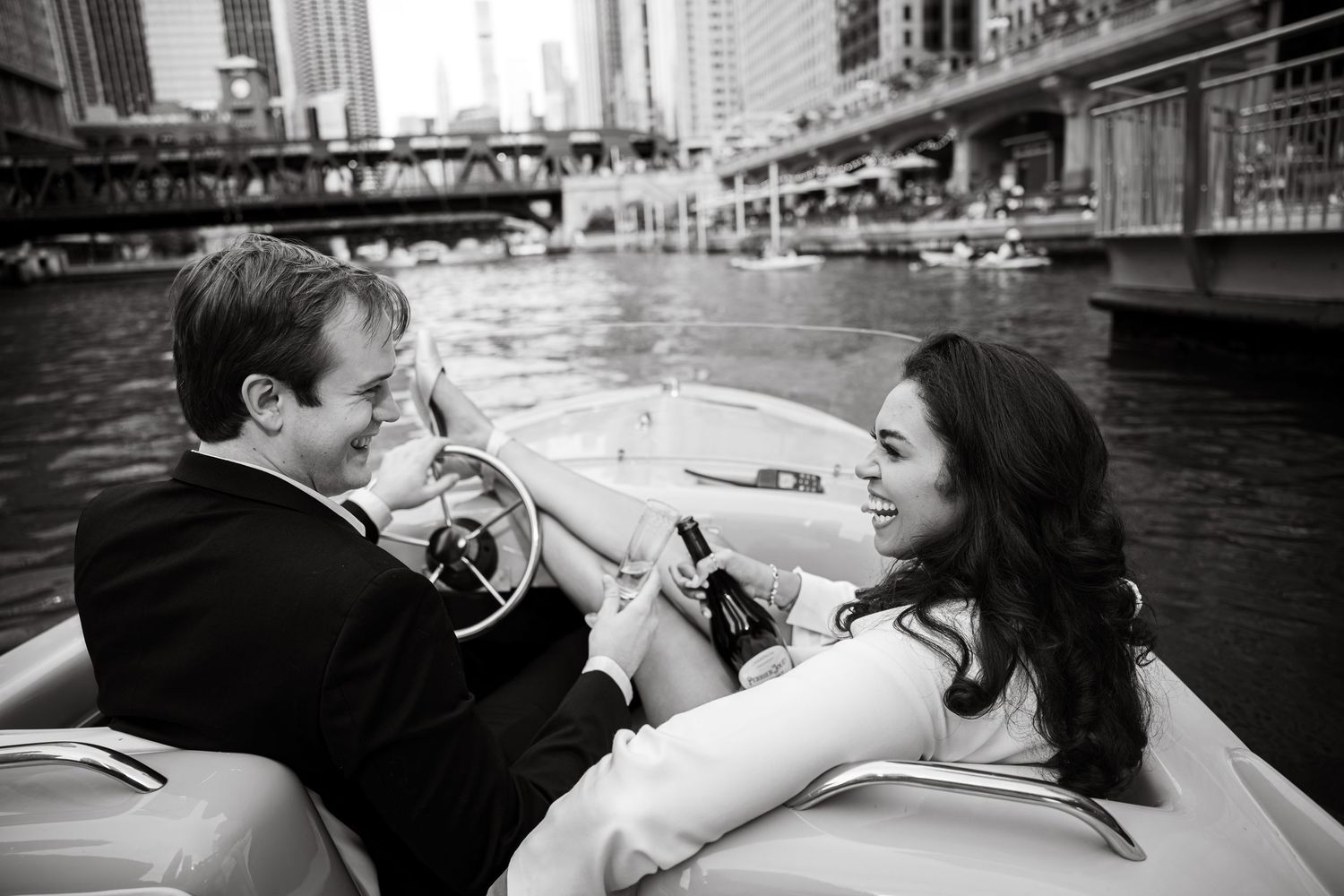 Couple enjoying champagne on a speedboat along a city river in black and white.