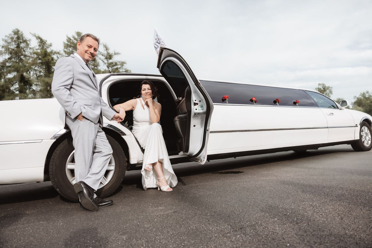 Bride and groom posing elegantly beside a white stretch limousine on their wedding day.