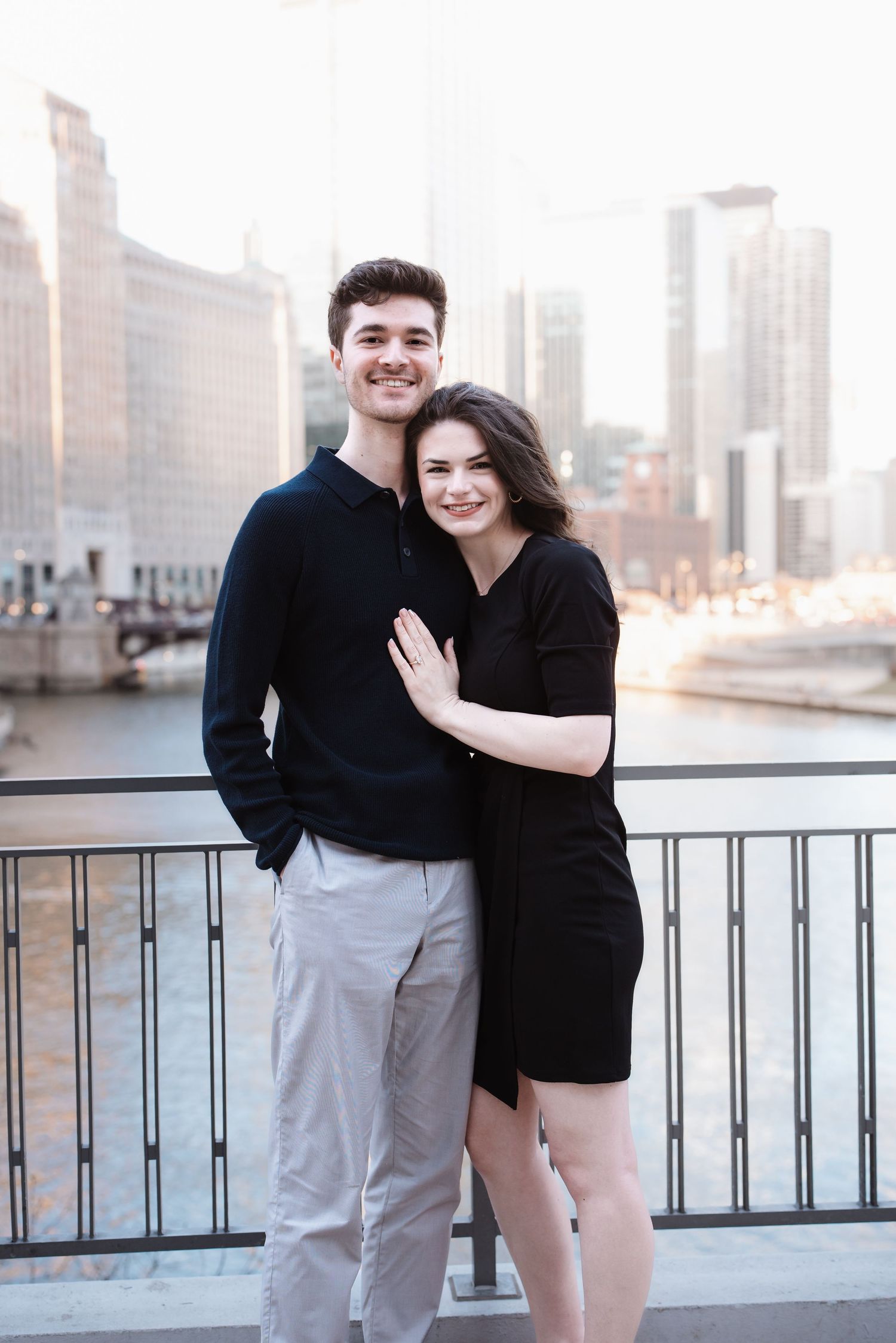 Happy young couple posing together on urban bridge with Chicago River and city skyline at sunset.