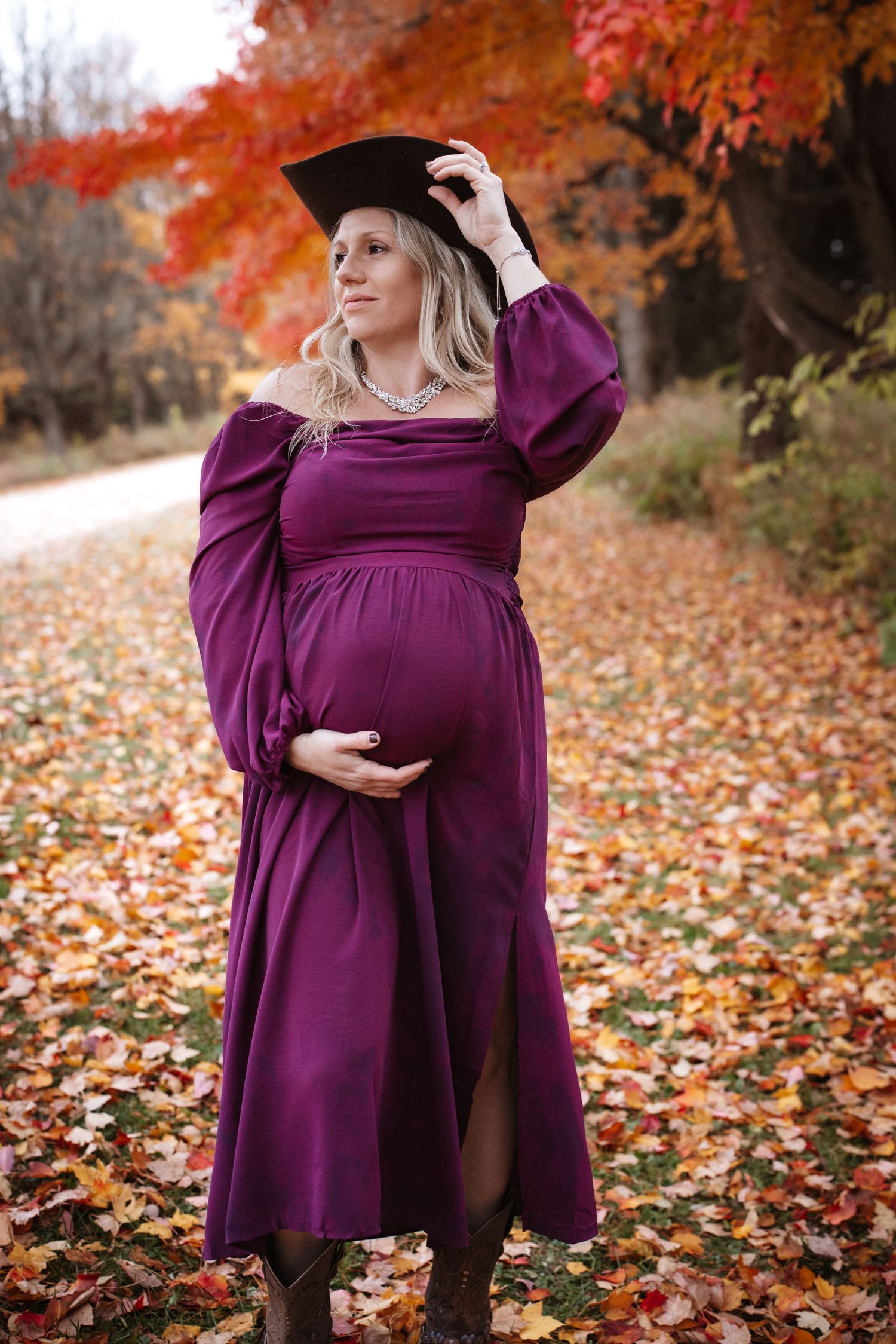 Pregnant woman in purple dress with graduation cap standing in autumn park.