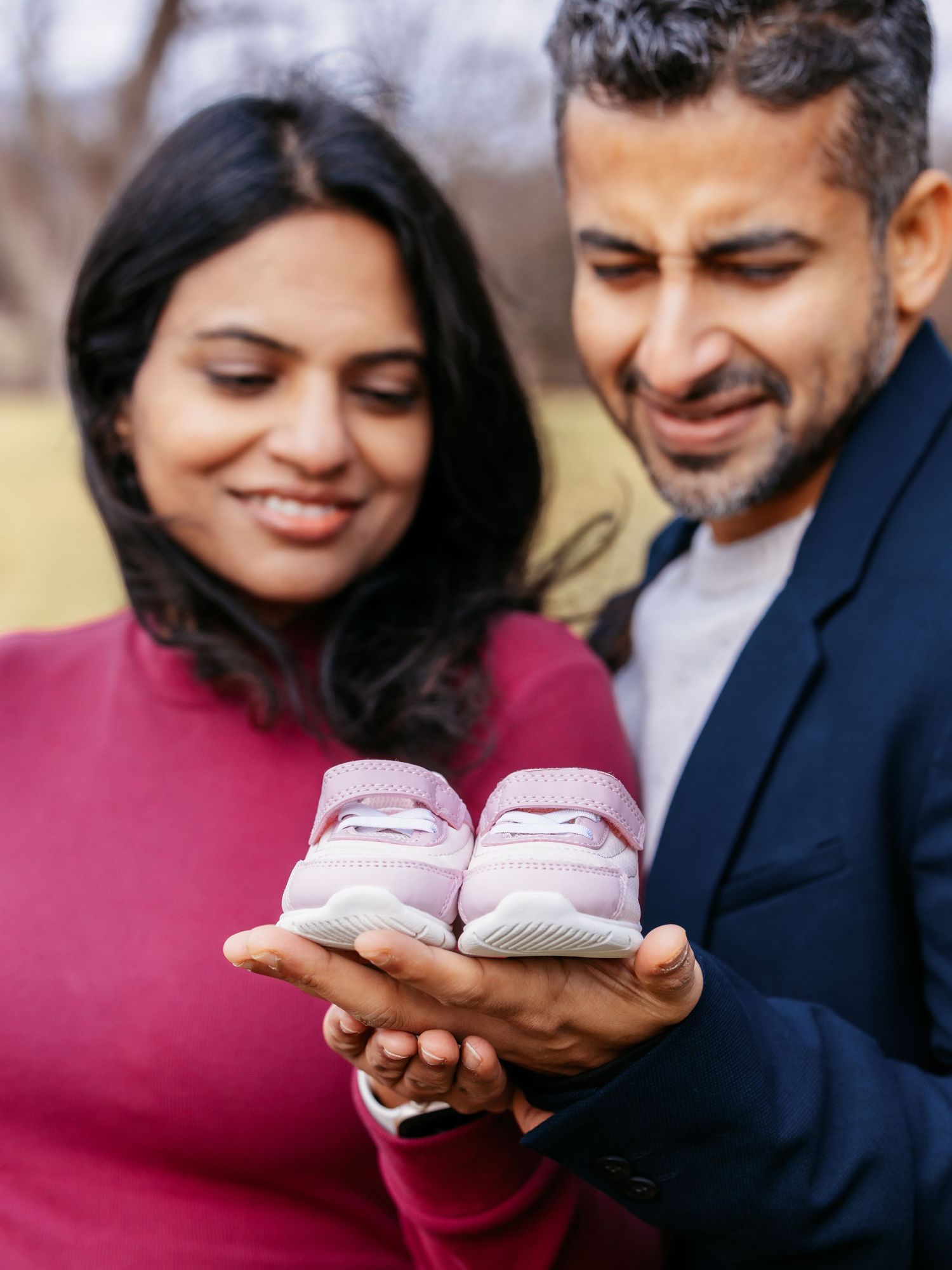 Close-up of expecting couple admiring tiny pink baby shoes held in their hands outdoors.