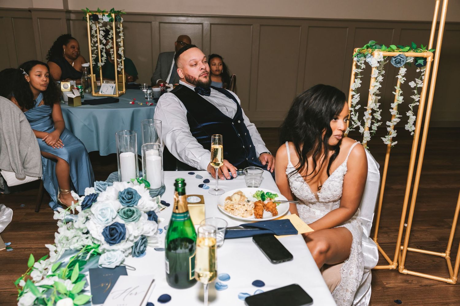 Bride and groom relaxing at sweetheart table with champagne and blue floral centerpieces.