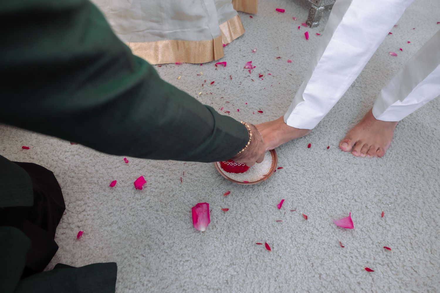 Traditional Indian wedding ritual with groom touching bride feet in plate of red vermillion petals.