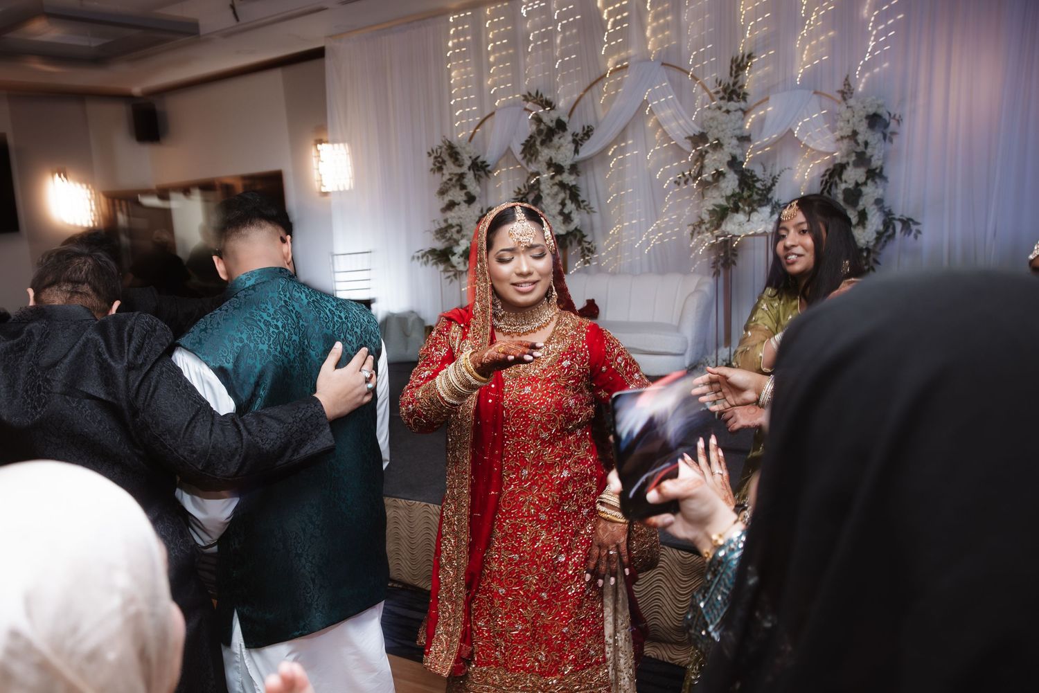 Bride in red traditional South Asian bridal attire greeting guests at wedding reception.