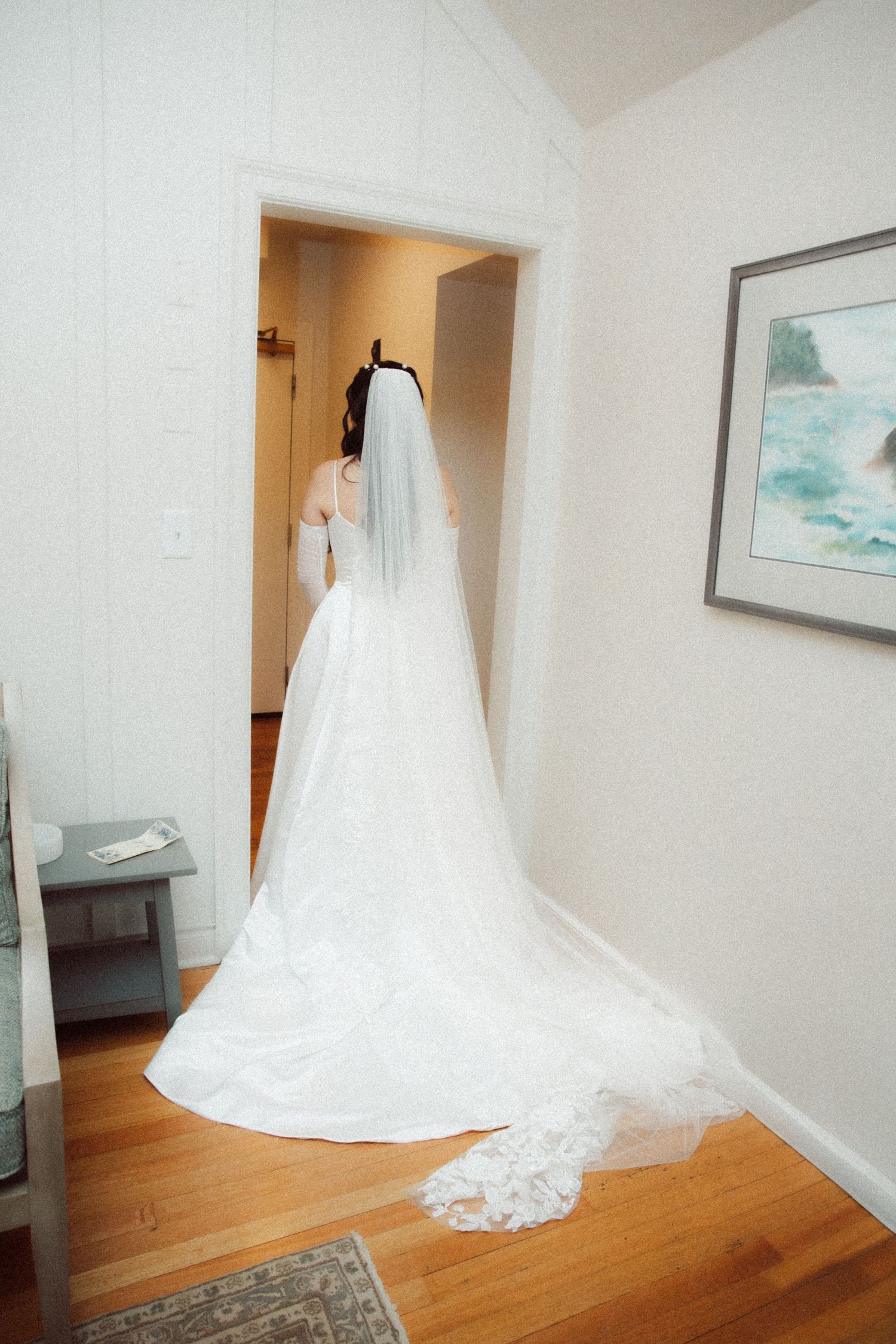 Bride in stunning ball gown wedding dress with lace cathedral veil stands in bright doorway before ceremony.