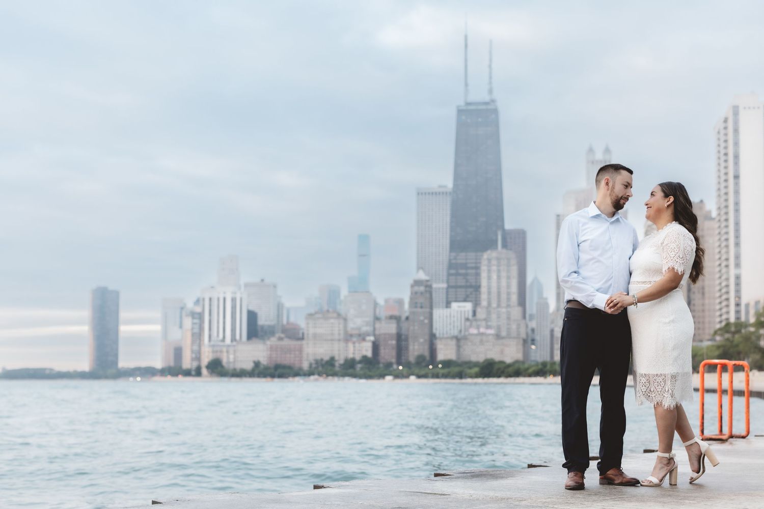 Engaged couple holding hands on a pier with the iconic Chicago skyline behind them.