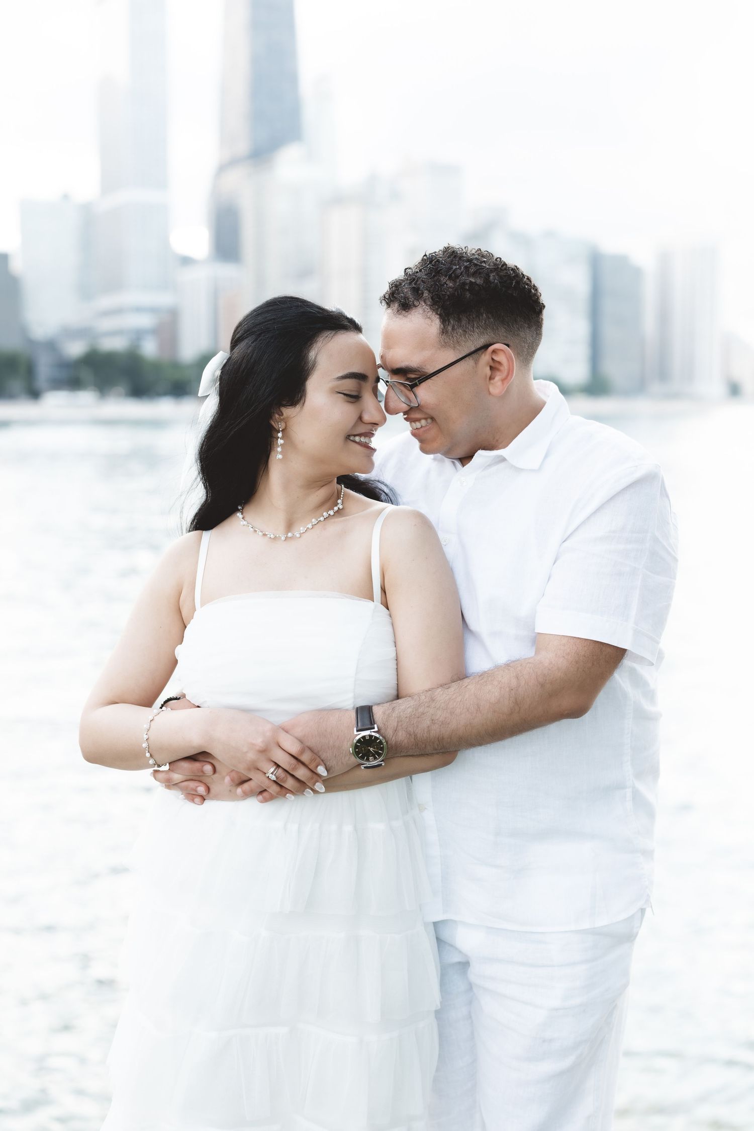 Couple in matching white outfits embracing by the waterfront with Chicago skyline in background.