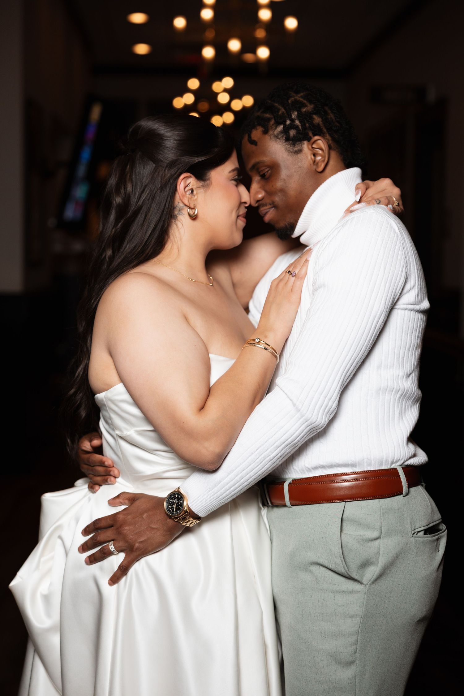 Bride and groom sharing romantic embrace under chandelier at wedding reception.