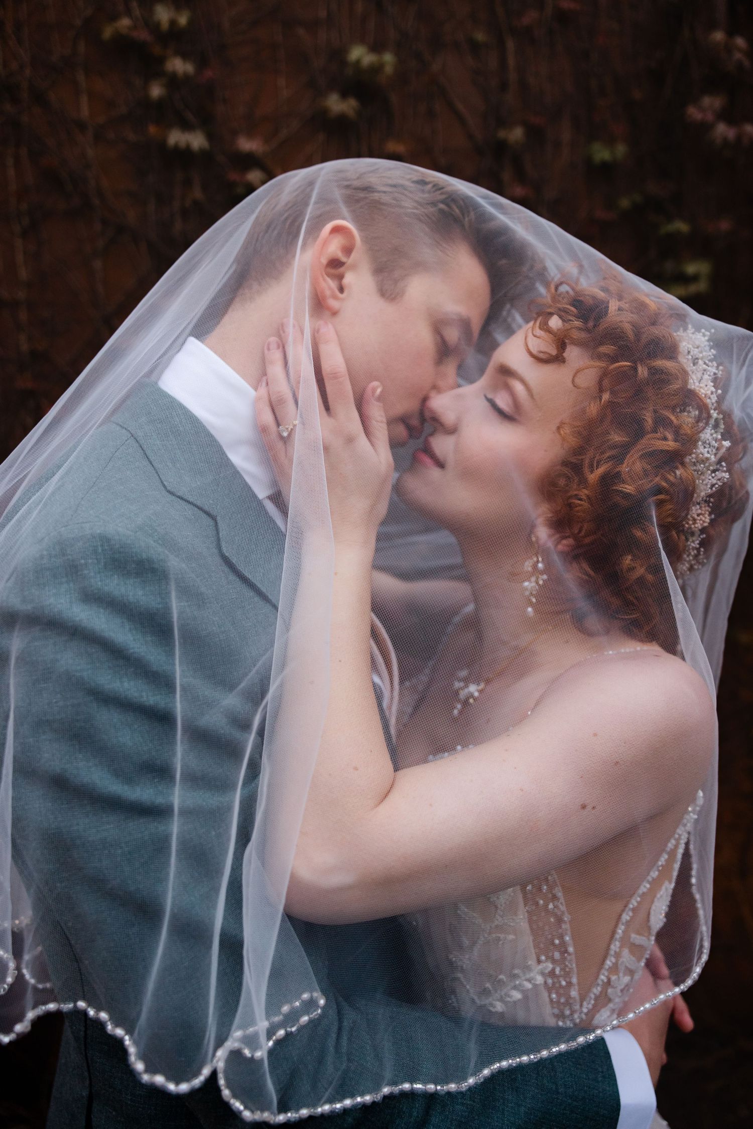 Bride and groom share a romantic kiss under a flowing white veil on their wedding day.
