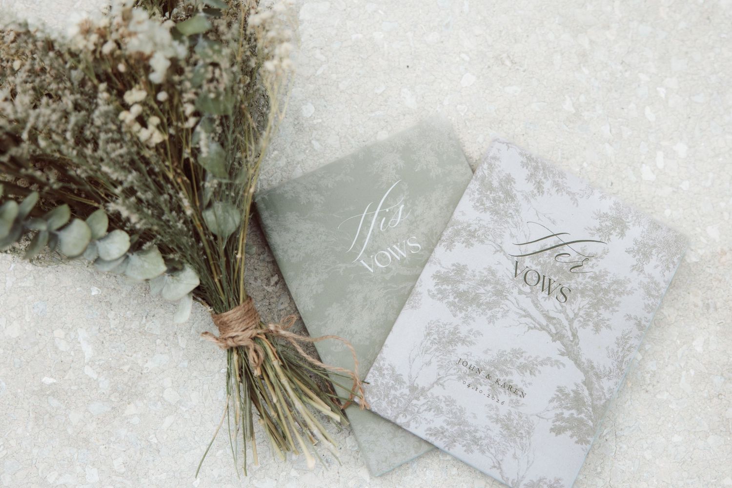 Elegant wedding stationery with floral design beside a dried flower bouquet on a white textured surface.