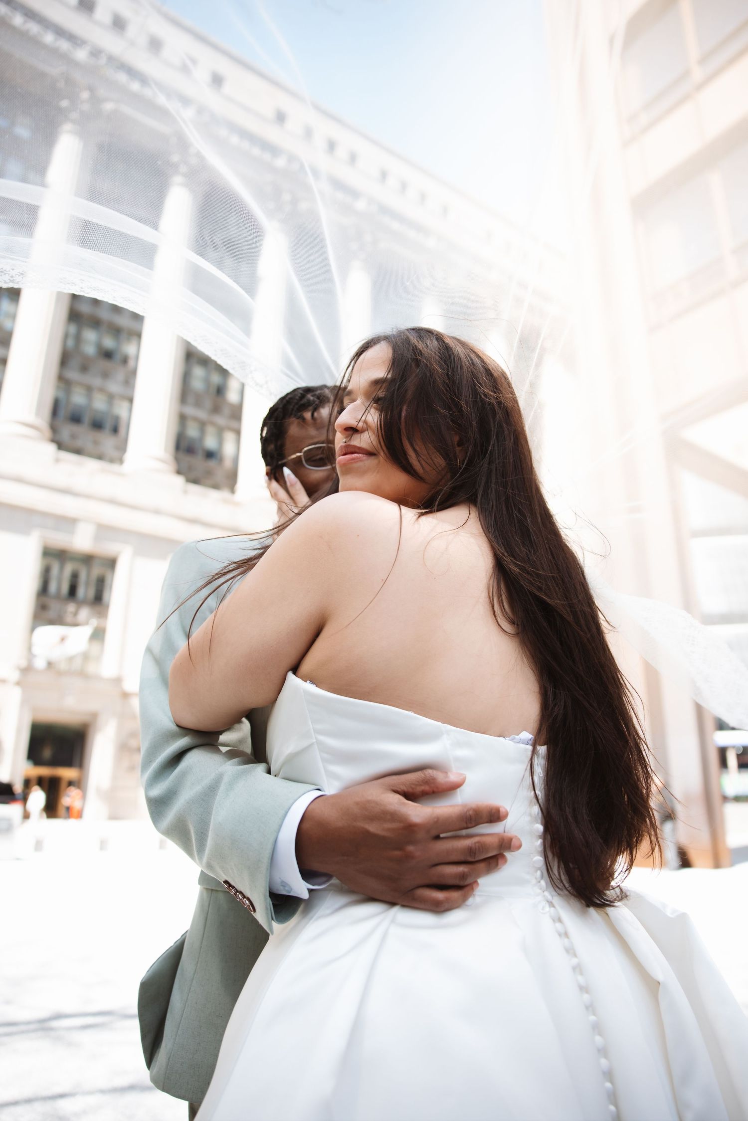 Bride and groom embracing outdoors in sunlight during wedding day portrait.