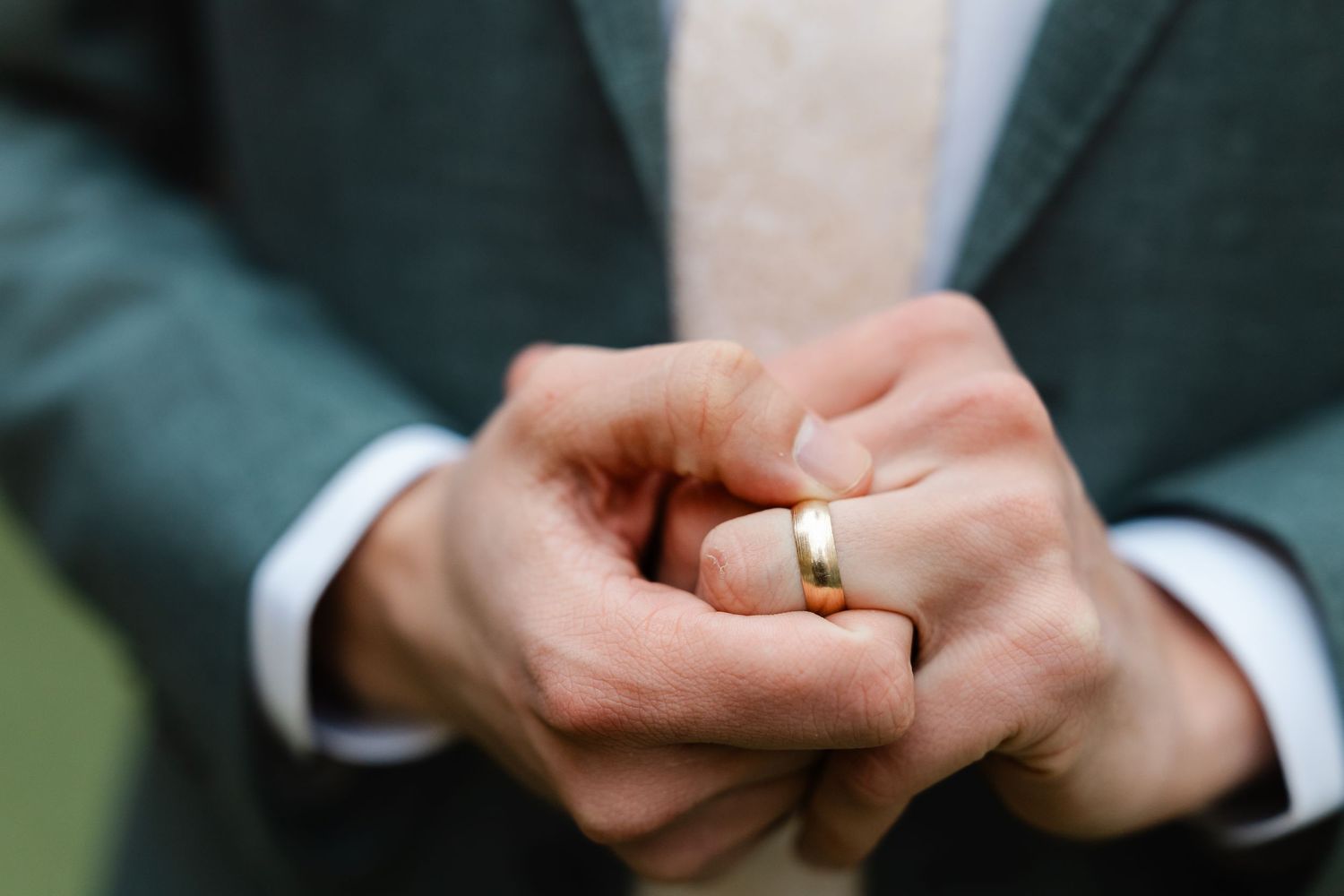 Close-up of grooms hands adjusting gold wedding band on finger after ceremony.