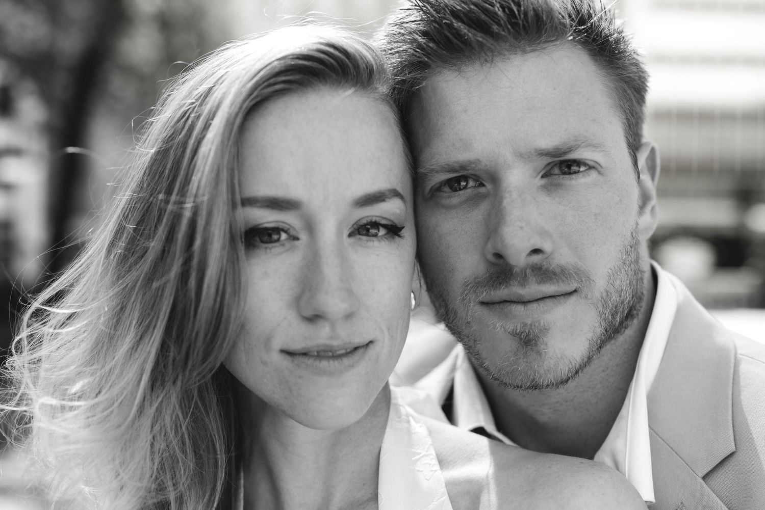 Close-up black and white portrait of a smiling couple outdoors, woman with blonde hair, man with stubble.