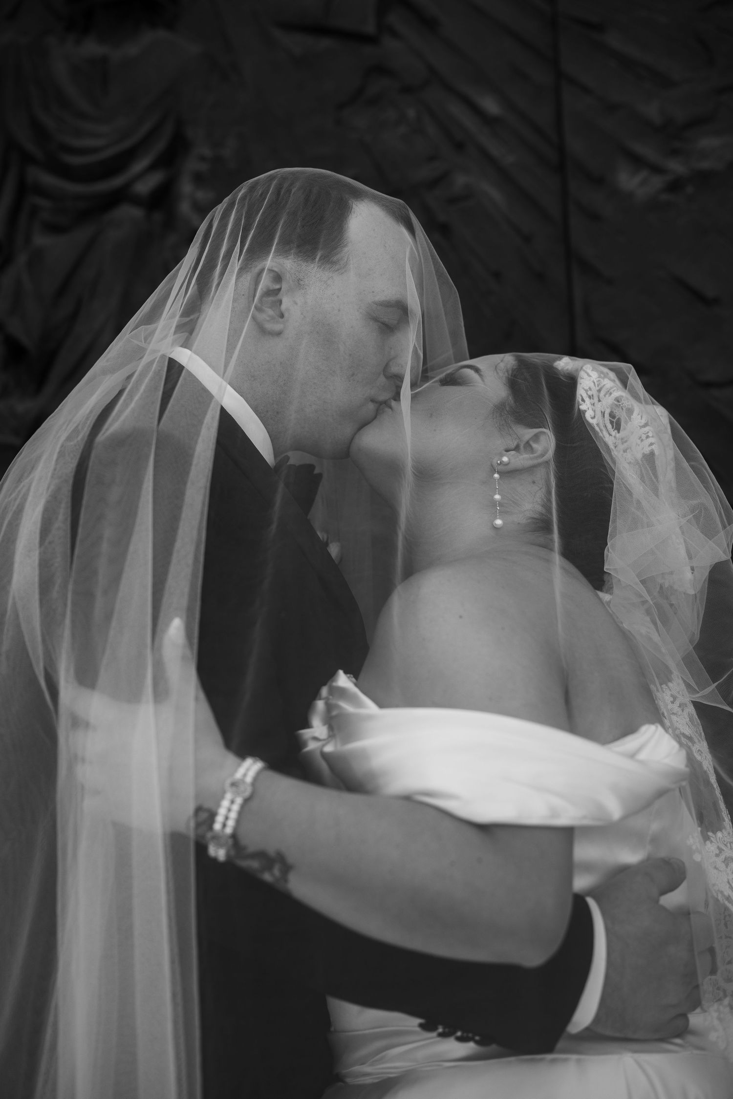 Black and white photo of bride and groom kissing under wedding veil.
