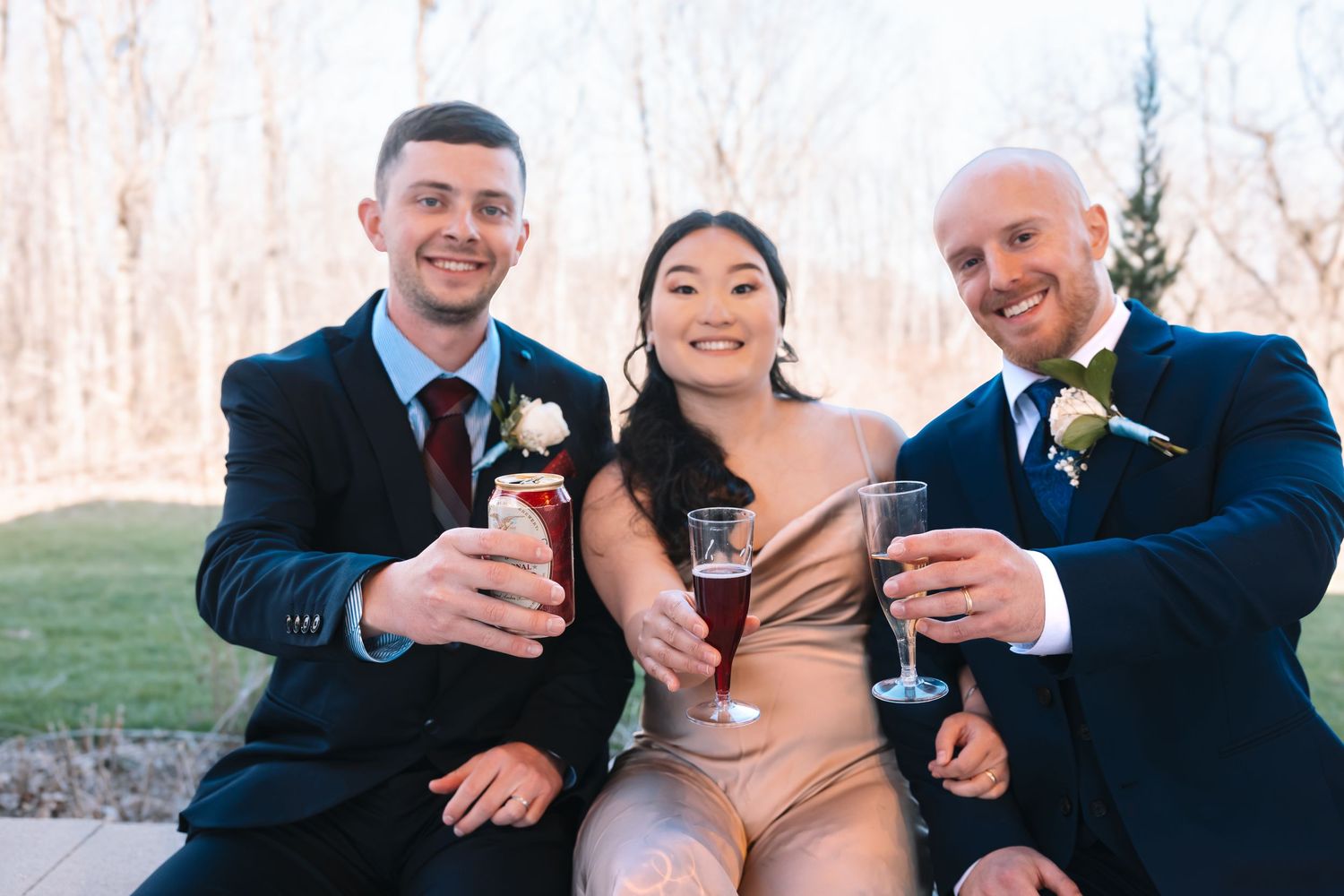 Three smiling wedding guests raising champagne glasses in a celebratory toast at an outdoor wedding.