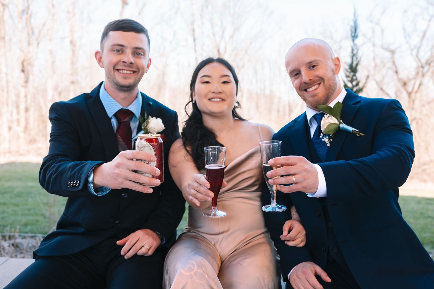 Two groomsmen and a bridesmaid in champagne dress toasting with wine glasses at a wedding reception.