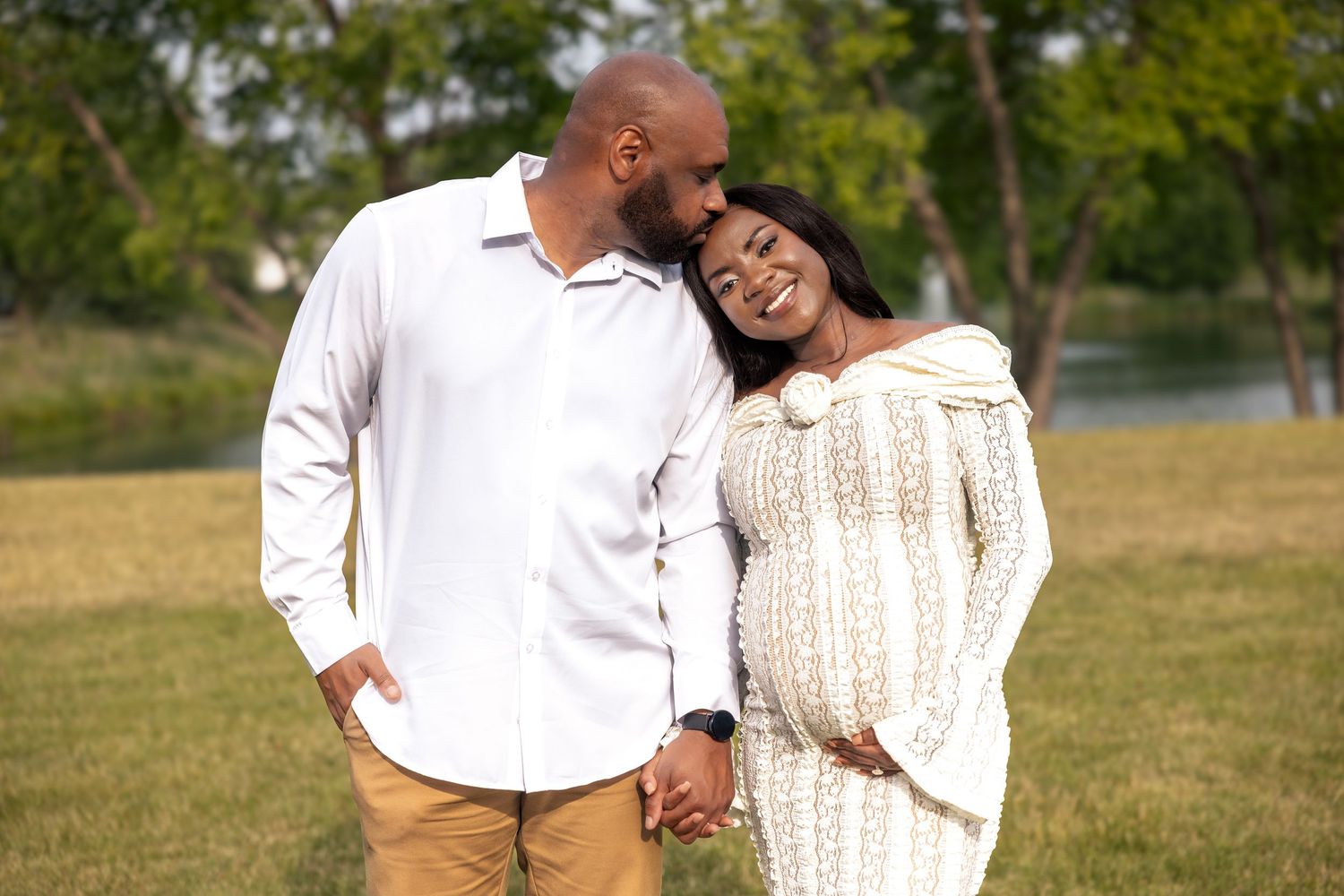 A happy pregnant couple holds hands and smiles in a park.